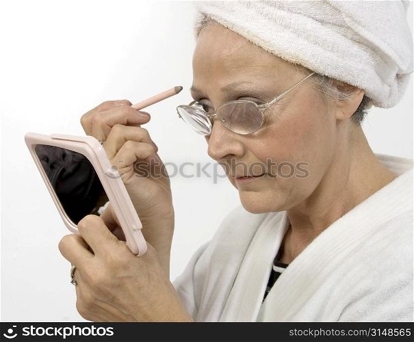 Woman in fifties appying make-up. Wearing white robe and towel in hair. Shot in studio.