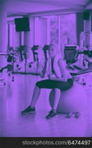 woman in fitness gym drink water. young healthy blonde woman drinking water in fitness gym while sitting on pilates ball duo tone