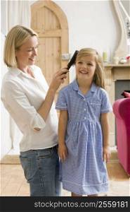 Woman in front hallway brushing young girl&acute;s hair and smiling