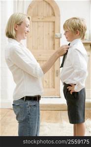 Woman in front hallway fixing young boy&acute;s tie and smiling