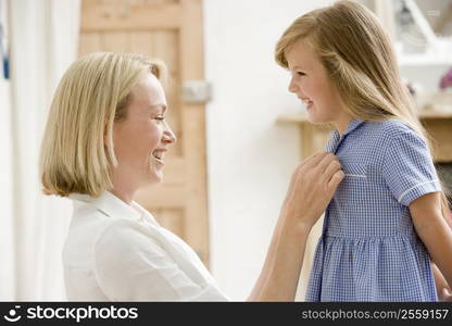 Woman in front hallway fixing young girl&acute;s dress and smiling