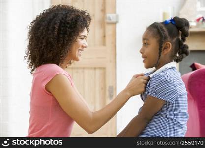 Woman in front hallway fixing young girl&acute;s dress and smiling