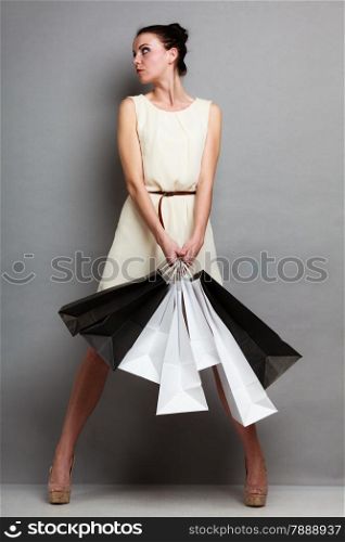 Woman in full length holding black white paper shopping bags. Elegant lady bright dress buying clothes. Sale and retail.