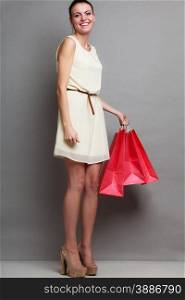 Woman in full length holding red paper shopping bags. Elegant lady bright dress buying clothes. Sale and retail.