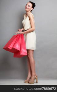 Woman in full length holding red paper shopping bags. Elegant lady bright dress buying clothes. Sale and retail.