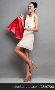 Woman in full length holding red paper shopping bags. Elegant lady bright dress buying clothes. Sale and retail.