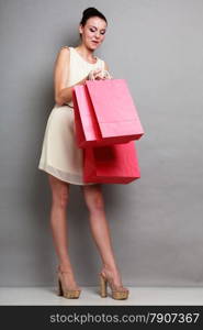 Woman in full length holding red paper shopping bags. Elegant lady bright dress buying clothes. Sale and retail.