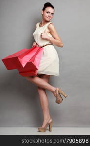 Woman in full length sale and retail concept. Girl with red shopping bags making thumb up hand sign gesture on grey background studio shot.
