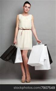 Woman in full length sale time. Girl with black and white shopping bags in hands on black over grey background in studio.