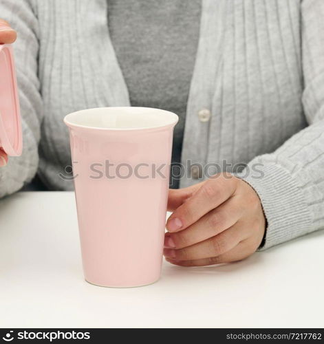 woman in gray clothes holds a pink ceramic cup, woman sits at a white table, start of the day, morning