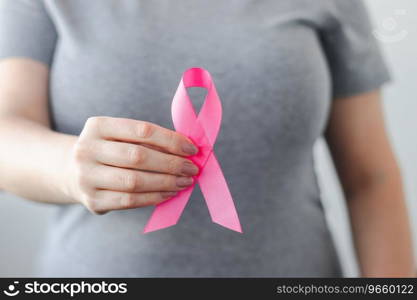 Woman in gray t-shirt holds pink ribbon in her hands. Breast Cancer Awareness Month. Supporting and promoting c&aign against cancer. Health care concept.. Woman in gray t-shirt holds pink ribbon in her hands. Breast Cancer Awareness Month. Supporting and promoting c&aign against cancer.