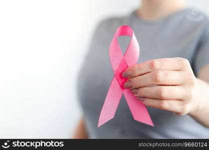 Woman in gray t-shirt holds pink ribbon in her hands. Breast Cancer Awareness Month. Supporting and promoting c&aign against cancer. Health care concept. Copy space.. Woman in gray t-shirt holds pink ribbon in her hands. Breast Cancer Awareness Month. Supporting and promoting c&aign against cancer.