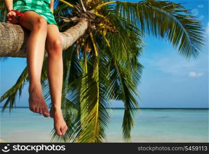 Woman in green dress sitting on a palm tree at tropical beach, Maldives