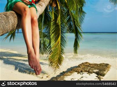 Woman in green dress sitting on a palm tree at tropical beach, Maldives