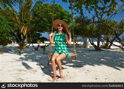 Woman in green dress swinging at tropical beach