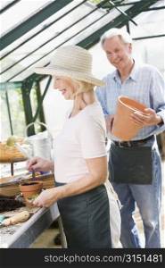 Woman in greenhouse planting seeds and man holding pot smiling
