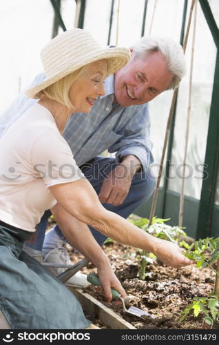 Woman in greenhouse planting seeds and man holding watering can smiling