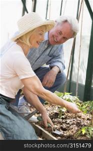 Woman in greenhouse planting seeds and man holding watering can smiling