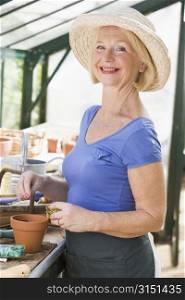 Woman in greenhouse putting seeds in pot and smiling