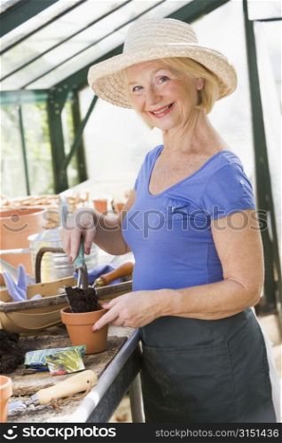 Woman in greenhouse putting soil in pot and smiling