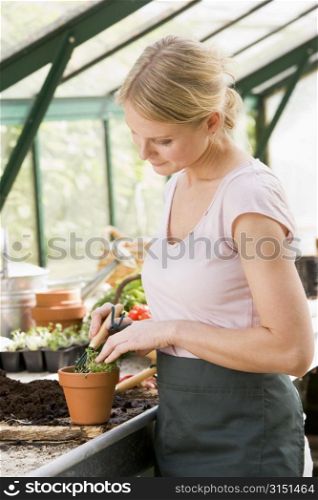 Woman in greenhouse raking soil in pot smiling