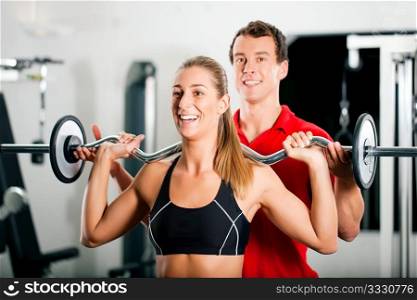 Woman in gym with personal fitness trainer exercising power gymnastics with a barbell
