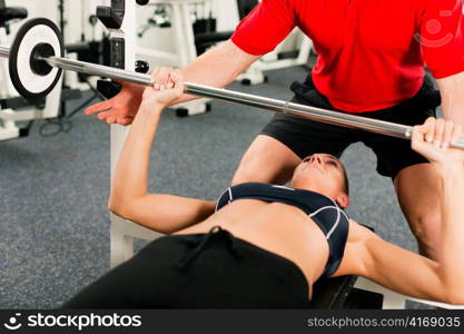 Woman in gym with personal fitness trainer exercising power gymnastics with a barbell