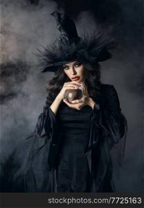 Woman in Halloween witch costume with crystal ball. Beautiful sexy model girl in sinister costume and make up. Halloween witch with crystal ball