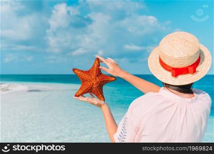 Woman in hat holding giant red starfish on white beach in the nature reserve. Adorable girl with starfish on the beach