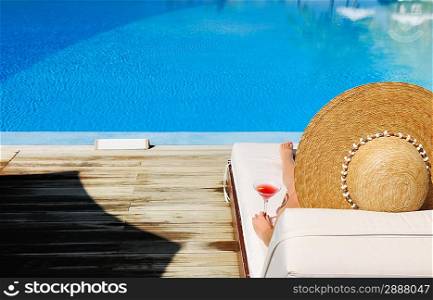 Woman in hat relaxing at the poolside with cosmopolitan cocktail