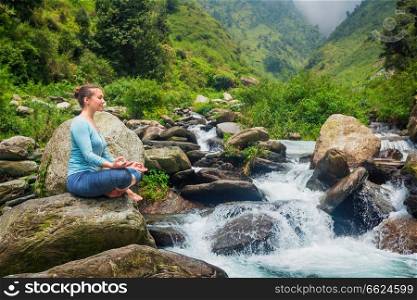 Woman in Hatha yoga asana Padmasana outdoors at tropical waterfall. Woman in Padmasana outdoors