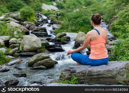 Woman in Hatha yoga asana Padmasana outdoors at tropical waterfall. Woman in Padmasana outdoors