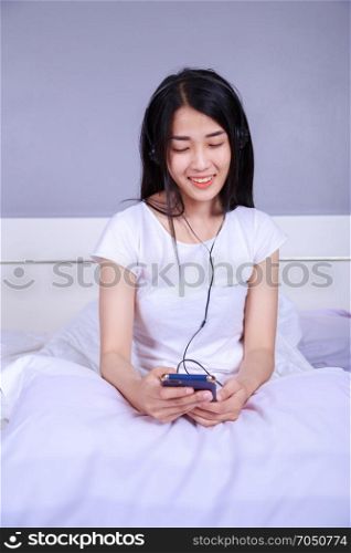woman in headphones listening to music from smartphone on bed in the bedroom