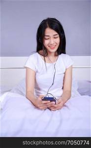 woman in headphones listening to music from smartphone on bed in the bedroom