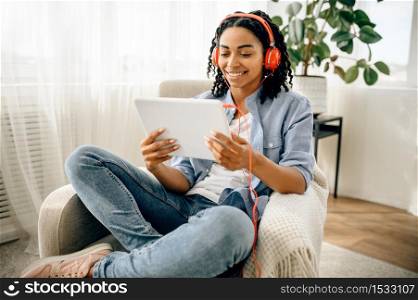 Woman in headphones listening to music from tablet pc. Pretty lady in earphones relax in the room, sound lover resting in armchair. Woman in headphones listening to music from tablet