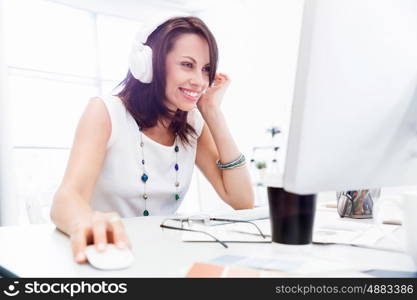 Woman in headphones sitting at desk in office. Woman in headphones