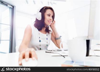 Woman in headphones sitting at desk in office. Woman in headphones