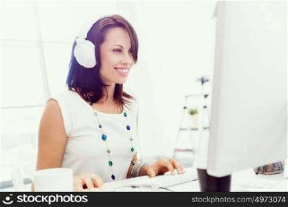 Woman in headphones sitting at desk in office. Woman in headphones