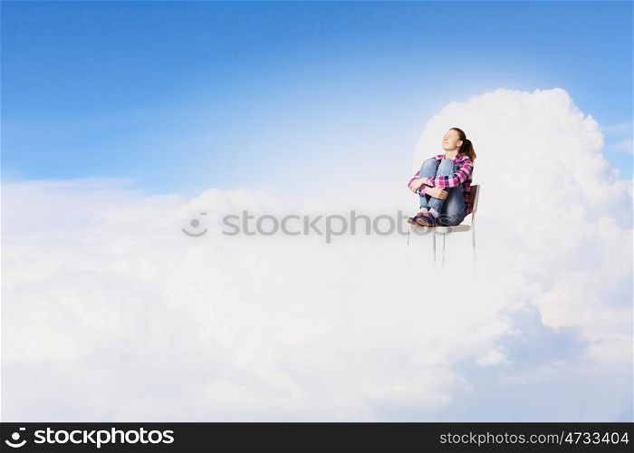 Woman in heaven. Young woman sitting in chair on cloud high in sky