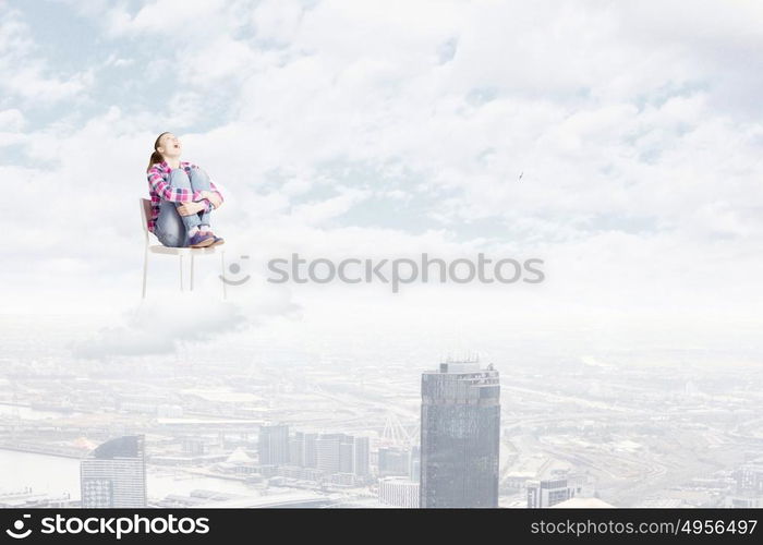 Woman in heaven. Young woman sitting in chair on cloud high in sky