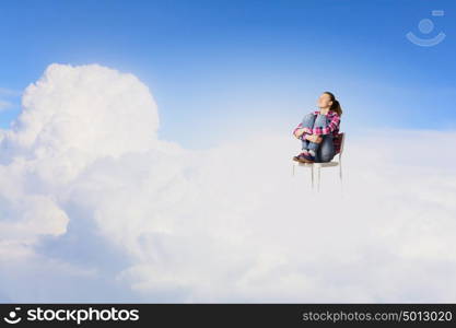 Woman in heaven. Young woman sitting in chair on cloud high in sky