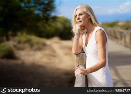 Woman in her 60s leaning on wooden fences on the sand of a tropical beach, enjoying her time of relaxation.. Woman in her 60s leaning on wooden fences on the sand of a tropical beach.