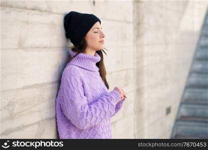 Woman in her twenties leaning against a wall outside with her eyes closed. Lifestyle concept.. Woman in her twenties leaning against a wall outside with her eyes closed.