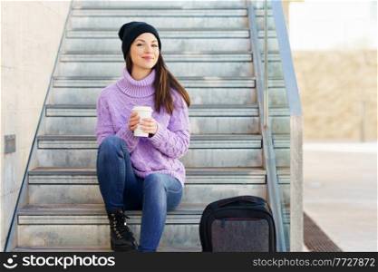 Woman in her twenties taking a coffee break sitting on some steps in the street. Lifestyle concept.. Woman in her twenties taking a coffee break sitting on some steps in the street.