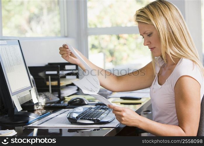 Woman in home office with computer and paperwork frowning