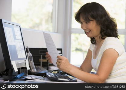 Woman in home office with computer and paperwork smiling