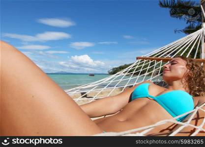 Woman in hummock on tropical beach. Young beautiful woman resting in hummock on tropical beach