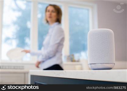 Woman In Kitchen Asking Digital Assistant Whilst Washing Up