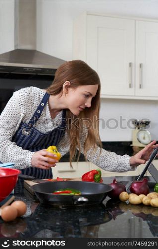 Woman In Kitchen At Home Following Recipe On Digital Tablet                             
