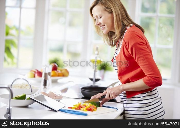 Woman In Kitchen Following Recipe On Digital Tablet